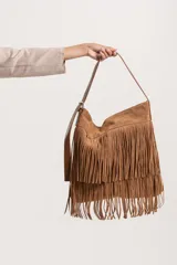Cartera de hombro color marrón, confeccionada en gamuza y eco-cuero. Presenta un diseño con doble capa de flecos largos en la parte frontal y correa ajustable.