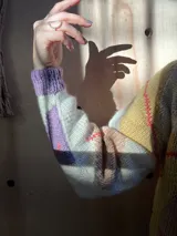 Cárdigan tejido de punto con diseño de rombos, en colores crema, violeta y detalles en rojo. Presenta cuello redondo, cierre frontal con botones de madera y textura acanalada en los bordes.
