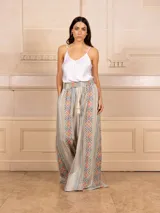 Pantalón tipo palazzo de corte amplio y fluido, con estampado geométrico étnico en tonos tierra, rosa y azul. Presenta cintura elástica con cordón ajustable y borlas decorativas.