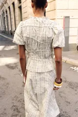 Blusa de manga corta abullonada con diseño a cuadros, cuello con volante y acabados elásticos. Cuenta con aberturas y lazos ajustables en los laterales.