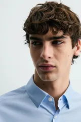 Camisa de corte slim fit, color negro, con cuello italiano, manga larga con puños abotonados y cierre frontal de botones. Confeccionada en tejido de fácil cuidado que minimiza la necesidad de planchado.