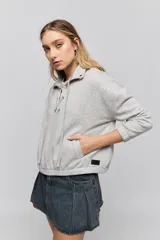 Buzo de calce relajado color tostado, con cuello alto y detalle de cordones entrelazados con ojales metálicos en el frente. Posee bolsillos laterales ocultos y puños y ruedo elastizados.
