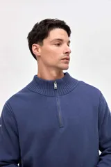 Buzo de punto color azul, con cuello alto y cierre frontal parcial. Presenta un diseño con textura acanalada en los hombros y mangas, y un pequeño bordado en la manga derecha.