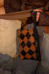 Cartera tipo sobre con diseño de ajedrez en rombos de cuero blanco y negro. Cuenta con una correa de mano integrada y detalle de placa metálica con logo.