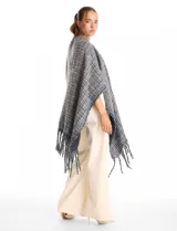 Ruana de tejido tweed en tonos verdes con destellos de lurex, diseño abierto con terminación de flecos en los bordes.
