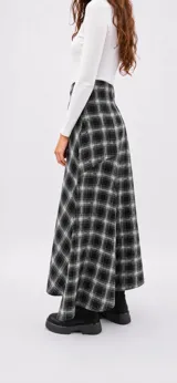 Falda midi de corte evasé con estampado de cuadros escoceses en tonos blanco y negro. Presenta un diseño con cortes asimétricos y cierre lateral.