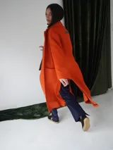 Tapado largo color naranja confeccionado en lana, con detalles en cuero. Tiene cuello con solapas, cierre frontal con botones ocultos, bolsillos laterales y corte holgado.