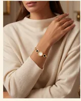 Pulsera de acero con baño de oro, compuesta por una cadena de eslabones y tres dijes circulares centrales, uno de nácar blanco y dos de ónix negro.