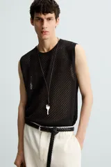 Chaleco de punto negro, con cuello redondo y manga sisa, confeccionado en tejido con estructura abierta (calado). Presenta bajo con aberturas laterales y acabados en rib.