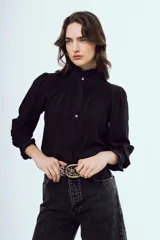 Camisa negra de manga larga con cuello alto gorguera y detalles fruncidos con nido de abeja en el pecho y los puños. Cierre frontal con botones.