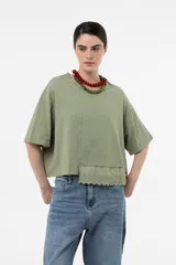 Remera verde militar de corte holgado y diseño amplio, con mangas cortas, hombros caídos, largo levemente cropped y detalle de broderie en el frente.