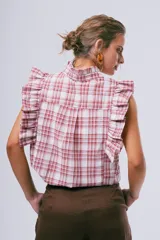 Blusa sin mangas color blanco con cuello alto con volados y detalles de volados en los hombros. Cuenta con cierre frontal de botones.