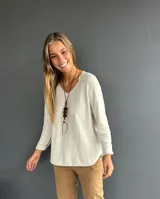 Sweater de tejido suave color crudo, con escote en V, manga larga y corte holgado con ruedo redondeado.