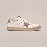 Zapatillas bajas de cuero vacuno blanco con aplique de estrella en cuero color aluminio y talón en cuero plateado. Cordones de algodón encerados color gris y suela de caucho con banda cosida. Plantilla de goma eva de 17 mm.