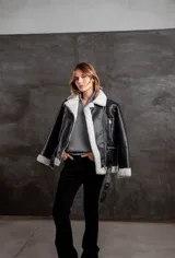 Campera tipo gamulán de eco cuero negro con interior y solapas de corderito sintético en color crudo. Presenta cierre frontal, bolsillos laterales con cierre y cinturón ajustable en la cintura.