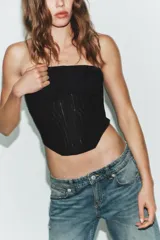 Corsé de escote strapless con detalle de drapeado en el pecho y varillas frontales visibles. Presenta un bajo asimétrico y cierre en la espalda.