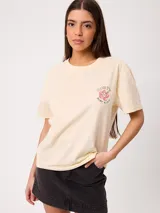Remera de manga corta Rusty, color beige, con ajuste holgado y estampado frontal pequeño de flor y texto.
