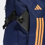 Mochila Adidas PrimeLift de color azul marino con detalles en naranja. Cuenta con compartimento principal con cierre, compartimento externo para notebook, bolsillos frontales y laterales, y correas de compresión laterales. El panel trasero es de malla para mayor ventilación.