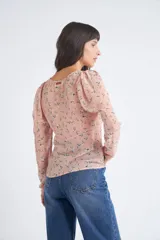 Blusa rosa con estampado de flores blancas y amarillas, cuello en V, manga larga abullonada y cierre frontal con botones.