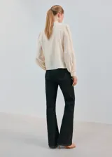 Blusa color crudo con cuello alto, detalles de bordados verticales en el frente y mangas largas abullonadas con puños ajustados.