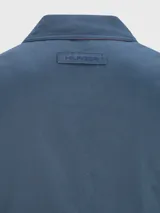 Campera azul con cierre de cremallera, cuello doblado, dos bolsillos inferiores a los lados, detalles distintivos de Tommy Hilfiger y logo de Tommy Hilfiger bordado en el pecho.