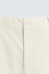 Pantalón chino de algodón color crema, corte regular fit, con cierre frontal de cremallera y botón, bolsillos delanteros y bolsillos traseros de vivo con botón.