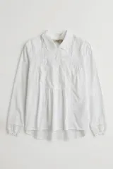 Camisa blanca de manga larga con detalles bordados en el frente, cuello redondo con solapas delicadas, cierre frontal con botones y puños anchos con encaje.