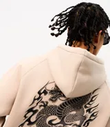Buzo canguro beige de algodón fleece con capucha y cordón ajustable. Presenta un bordado frontal con el texto "Forged by Fire" en tipografía estilo gótico con bordes rojos y negros.