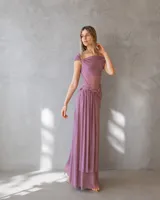 Vestido largo color malva con escote barco, cuerpo ajustado y falda fluida con detalle de drapeado y fruncido en la cintura.