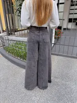 Pantalón de jean estilo wide leg en color gris oscuro con efecto lavado. Presenta un corte de tiro alto, costuras verticales marcadas en el frente y una silueta amplia y fluida.