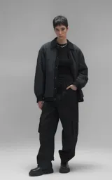Campera tipo sobrecamisa de diseño oversize, confeccionada en microfibra opaca con patrón matelaseado geométrico. Presenta cuello, puños, cartera central y ruedo en gabardina de algodón, con cierre frontal mediante broches a presión. El diseño del ruedo simula una prenda superpuesta.