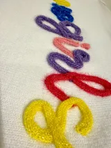Sweater de punto de manga corta en color blanco, con cuello redondo en color turquesa, puños en colores amarillo y rojo, y borde inferior en color fucsia. Presenta la palabra 'cowgirls' bordada en relieve con letras multicolores.
