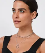 Conjunto de aros rectangulares plateados y collar a capas con cadena de eslabones cortos y cadena fina con colgante rectangular.