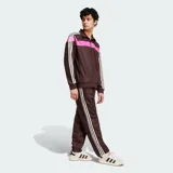 Pantalón deportivo Adidas color marrón, con diseño de monograma grabado en relieve en todo el tejido, franjas laterales blancas y el logo de la marca bordado en la cadera.