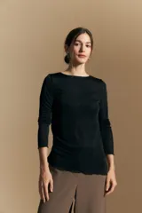Top de manga larga con textura suave y leve brillo. Presenta una silueta al cuerpo, tajos laterales y terminaciones onduladas en el ruedo.
