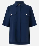 Camisa color fucsia de tejido airflow, con cuello camisero, mangas cortas con pliegues, cierre frontal con botones metalizados y bolsillos con solapa en el pecho.