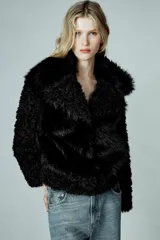 Abrigo corto de Zara Woman Collection con cuello de solapa y manga larga. Presenta una combinación de texturas con aplicación de pelo sintético y diseño de efecto rizado en mangas y bordes. Cuenta con forro interior y cierre frontal mediante ganchos metálicos.