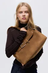 Bolso tote de acabado suave, color marrón, con asas tubulares unidas por una trabilla con hebilla metálica. Presenta una correa decorativa frontal con hebilla metálica y compartimento interior con cierre.