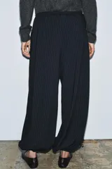 Pantalón de tiro medio, color negro con rayas diplomáticas finas blancas. Cintura elástica ajustable con cordones y bajo abullonado con elástico.