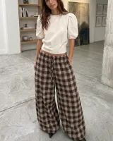 Pantalón de corte amplio y holgado con estampado de cuadros en tonos marrones y beige. Presenta cintura elástica con cordón de ajuste y diseño de tiro medio.
