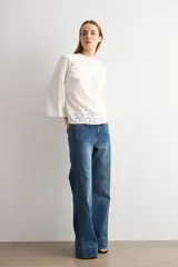 Blusa blanca de algodón con diseño de encaje bordado tipo broderie en el cuello, mangas y ruedo. Presenta mangas tres cuartos acampanadas y un corte holgado.