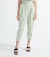 Pantalón color verde claro, de corte clochard, con cintura alta, pliegues frontales y bolsillos laterales.