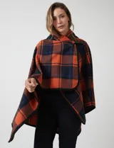 Capa de tejido cuadrille con diseño de cuadros en tonos marrón, beige y naranja. Presenta un cierre frontal con botón tipo trenca y bordes con ribete negro.