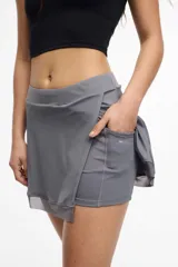 Falda short deportiva color violeta, con calza interna y bolsillo lateral. Presenta un frente cruzado y detalle de microtul en el dobladillo.