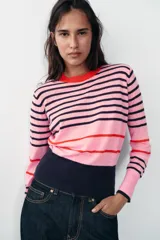 Jersey de punto de cuello redondo y manga larga con puños ajustados. Presenta un diseño de rayas horizontales en tonos rosa, azul marino y detalles en rojo.