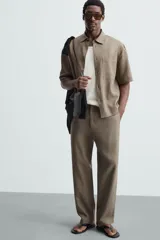Pantalón de calce relajado confeccionado en tejido de viscosa y yute color tostado. Presenta cintura elástica ajustable con cordón, bolsillos laterales, bolsillos traseros de vivo y cierre frontal con cremallera y botón.