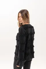 Blusa negra plisada de manga larga con detalles de volados horizontales en el frente y las mangas.