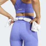 Calza de running ajustada de tiro alto, color lila/lavanda, con tecnología AEROREADY y tejido Adiflex. Presenta bolsillos laterales y detalles reflectantes, incluyendo el logo de Adidas en la parte inferior de la pierna.