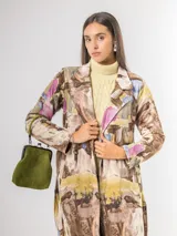 Trench de diseño urbano con acabado agamuzado, de corte recto y largo midi. Presenta un estampado abstracto multicolor con tonos rojizos, azules y ocres, cuello solapa, mangas largas y cinturón ajustable en la cintura.