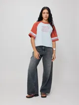 Remera bicolor Rusty con cuerpo verde lima y mangas ranglán grises con dos rayas blancas en los puños. Estampado frontal con el logo de la marca y el número 85.